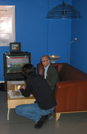 Figure 3: Two users listening to podcast shows at one listening station. The TV screen shows the waiting list (some users off-picture) and sound comes from the directed speaker hanging from the roof.